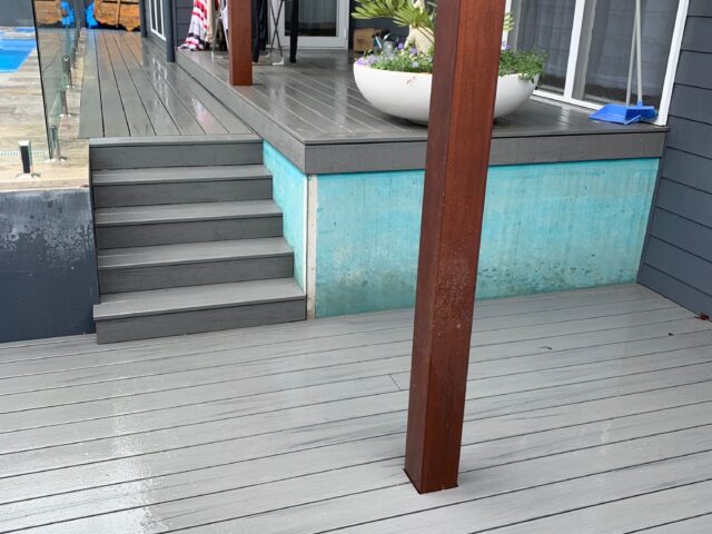 Wet grey composite deck with steps, timber posts, glass pool fence, sliding doors.