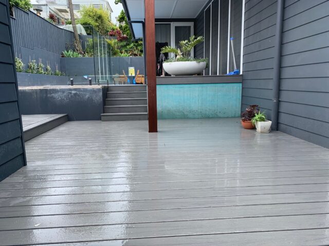 Wet grey composite deck with steps to raised terrace, glass balustrade and potted plants.