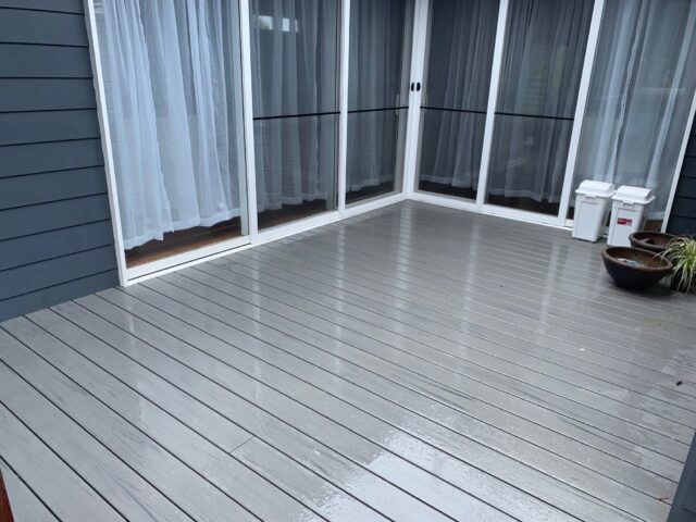 Grey composite decking outside sliding glass doors with dark cladding and planters.