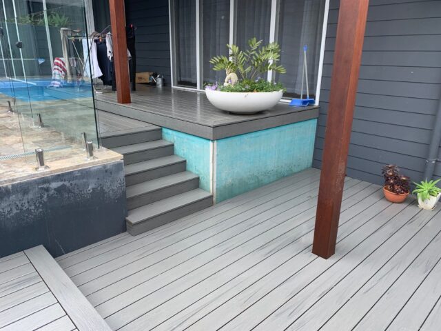 Grey deck with steps, glass pool fence, timber post and large bowl planter.