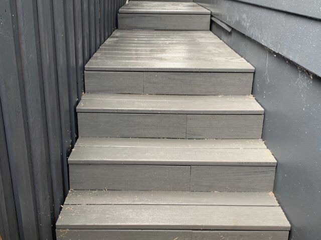 Outdoor composite decking steps in narrow side access between fence and cladding.