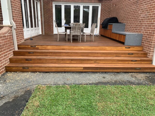 Timber deck with wide steps, outdoor dining, built-in barbecue, white French doors.