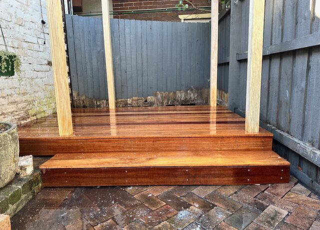 Hardwood deck with front step and pergola posts in a small courtyard.