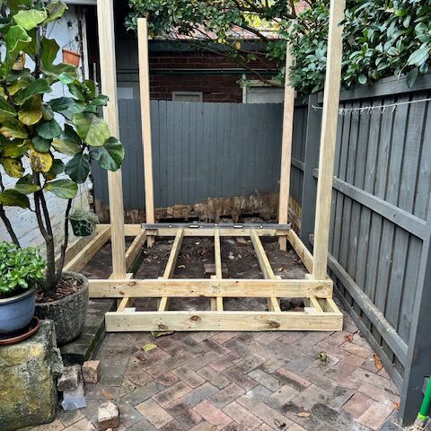 Timber deck subframe and posts under construction in narrow courtyard.