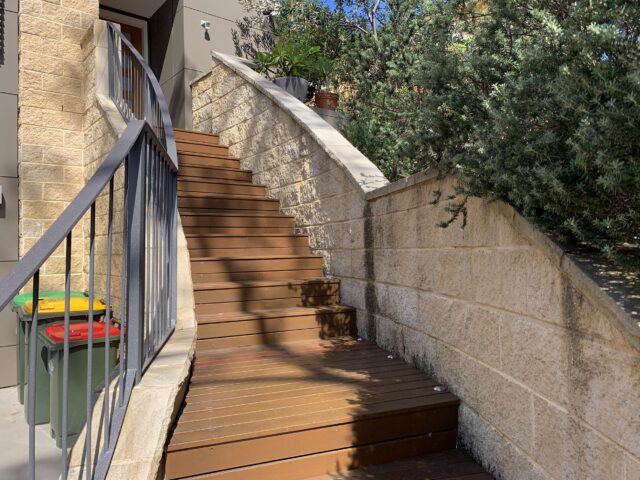 Outdoor timber stairs with steel railing and sandstone retaining walls to front entry.