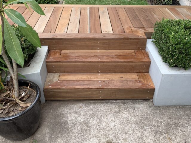 Timber deck and steps between rendered planters, opening to lawn and garden.