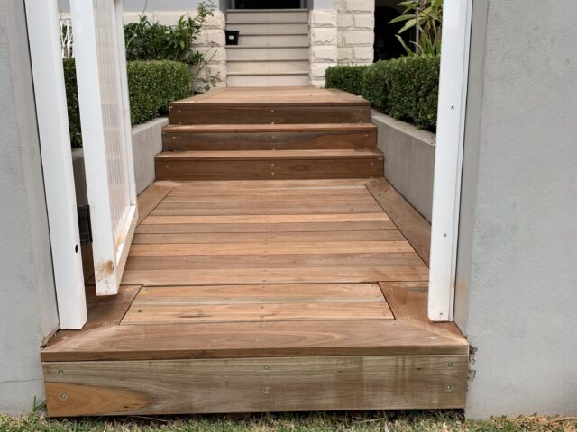Timber front deck and steps framed by low hedges, leading to home entrance.