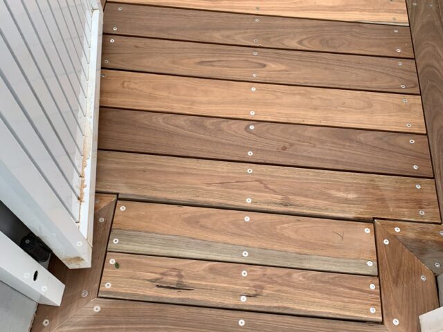 Hardwood decking with mitred picture-frame border beside a white gate and lawn.