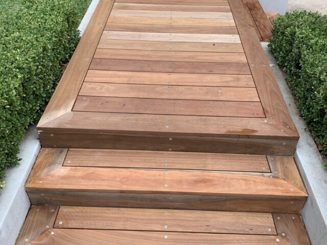Timber decking steps and raised walkway leading to front entry, hedges alongside.