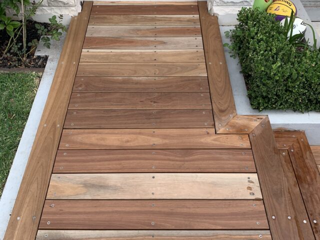 Hardwood decking walkway with mitred edges and stainless fixings leading to stone entry steps, garden beds.