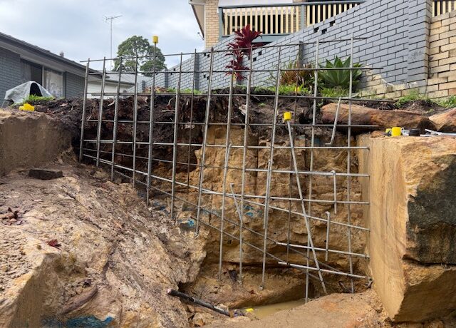Residential backyard excavation in sandstone with steel mesh for retaining wall.