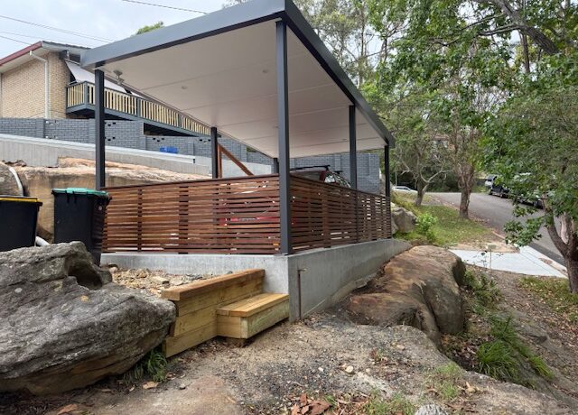 Covered deck with steel posts and timber slat screening on a landscaped rocky slope.