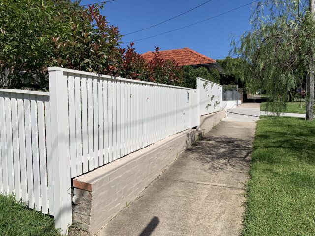 White vertical slat boundary fence on low brick wall beside footpath and driveway.