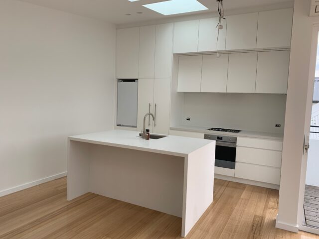 White kitchen with island sink, skylight, timber floors, gas cooktop and built-in oven.