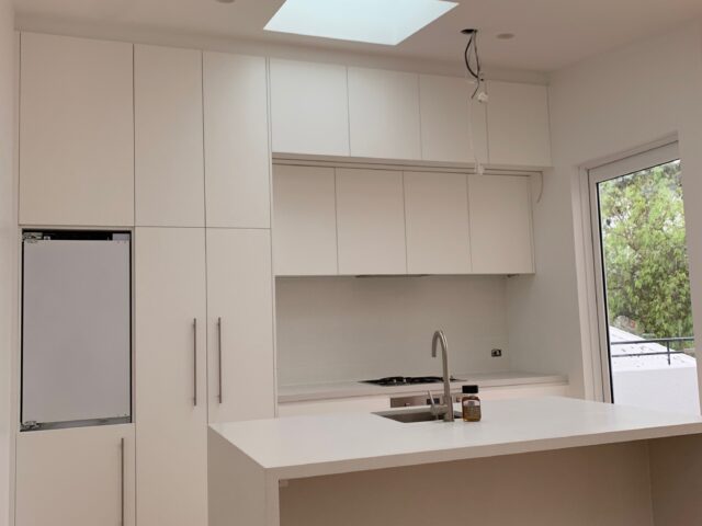 Light-filled modern kitchen with skylights, island bench sink, timber flooring, full-height cabinets.
