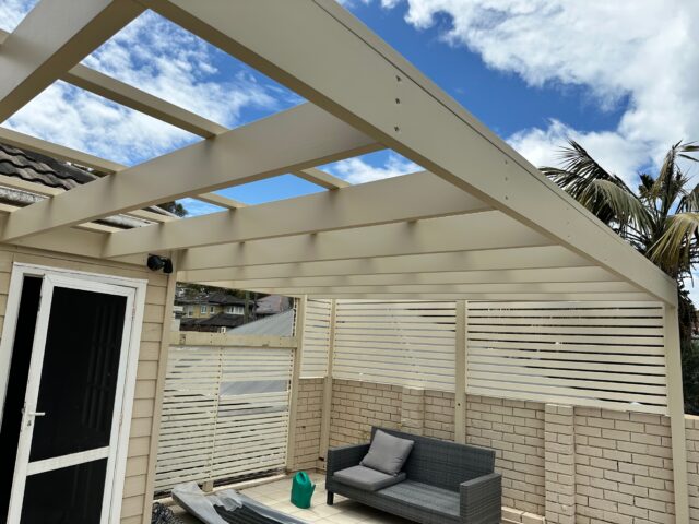 Timber pergola frame and slatted privacy screens over tiled patio seating.