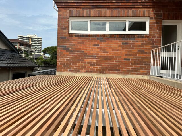 Slatted timber pergola roof under construction beside red brick home.