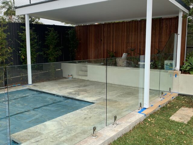 Covered poolside pergola, tiled paving, frameless glass fence, bamboo privacy screen.