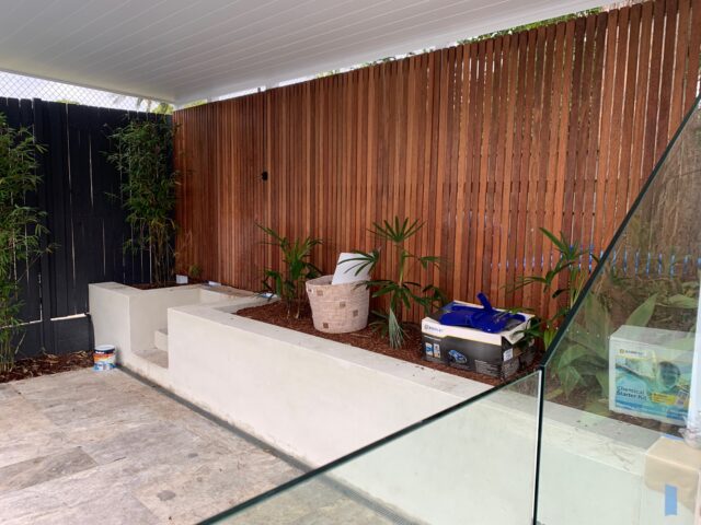 Covered patio with timber privacy screen, rendered planters, stone pavers and glass pool fence.