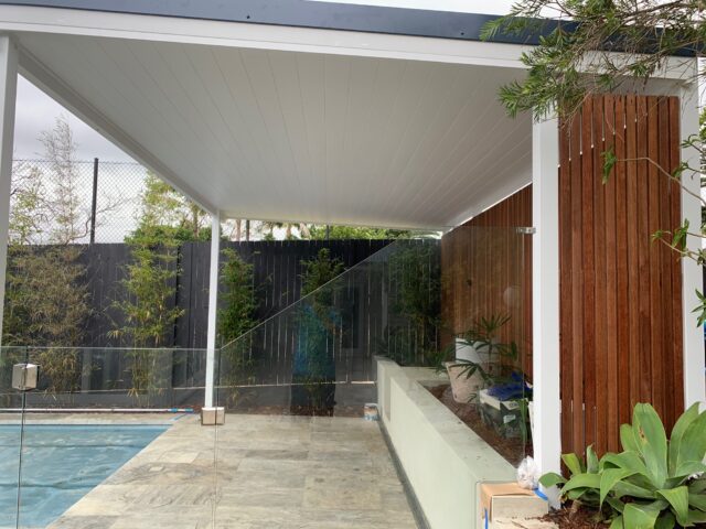 Poolside pergola with white ceiling, glass pool fence, timber privacy screen, and tiled patio.