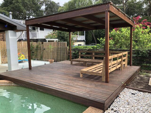 Timber poolside deck with pergola, bench frames, glass pool fence and garden.