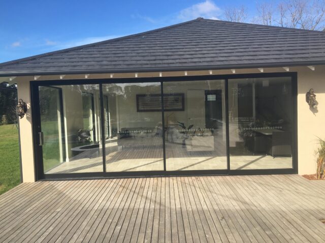 Timber deck opening to wide black-framed sliding glass doors on modern extension