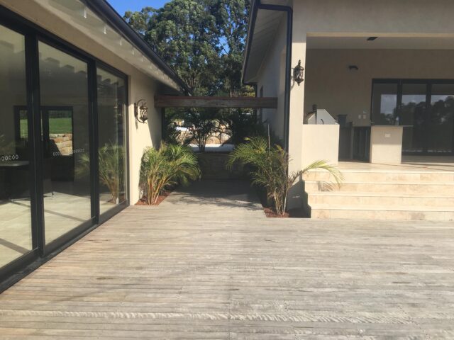 Timber deck with potted palms, sliding doors, and steps to covered outdoor kitchen.