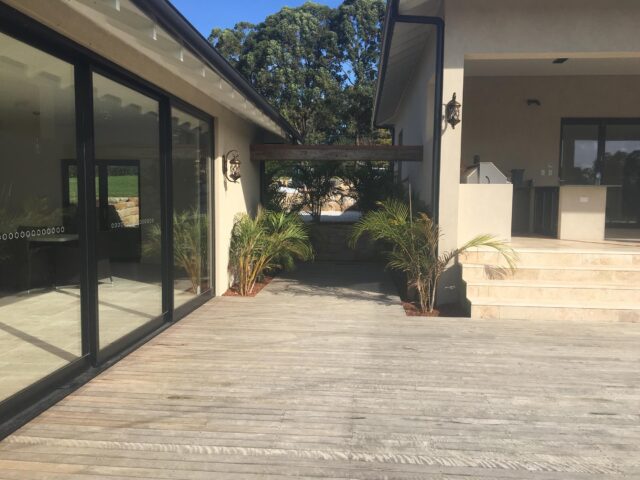 Timber deck between sliding doors and tiled steps to covered outdoor kitchen, potted palms.