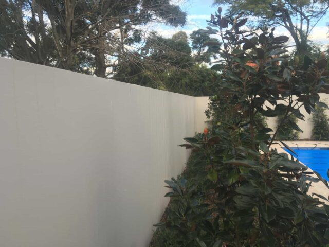 Light-coloured privacy fence with hedge planting beside a covered backyard pool.