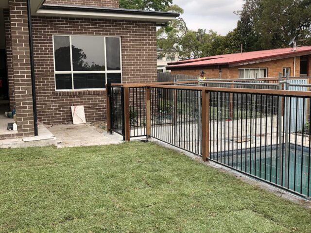 Backyard renovation with new lawn and timber-steel pool fence at brick house.