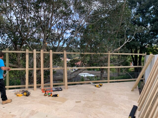 Timber privacy screen frame under construction on a tiled patio, builder and tools.