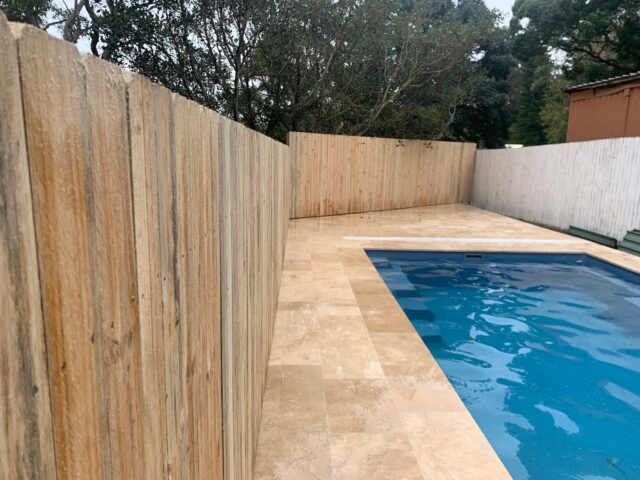 Rectangular pool with light stone paving and freshly installed timber fencing.