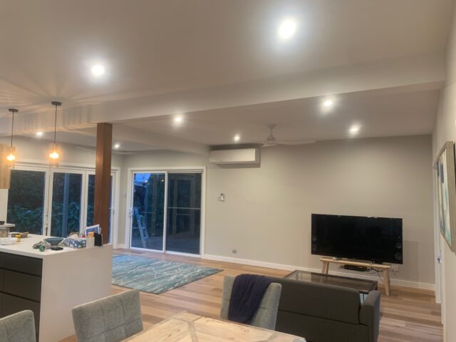 Open-plan living and kitchen with recessed and pendant lighting, sliding doors, timber flooring.