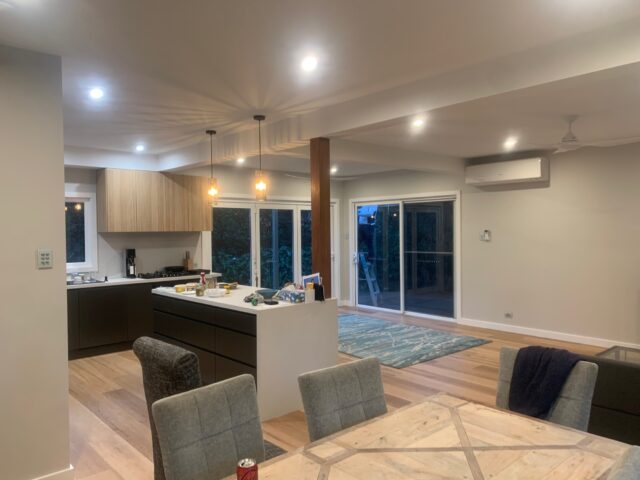 Modern open-plan kitchen and dining with island bench, timber floors, sliding doors to deck.