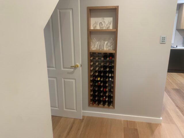 Recessed wine rack with timber surround and glassware shelves in hallway.