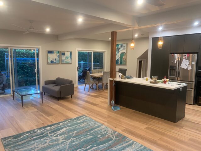 Open-plan kitchen and living with timber floors, pendant lights, and sliding doors to deck.