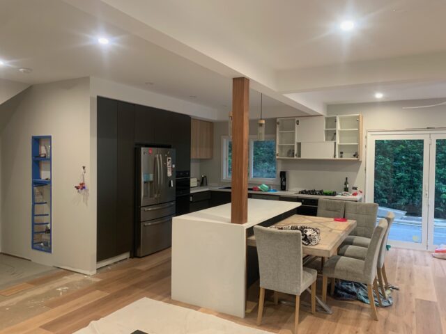 Kitchen-dining renovation with new cabinetry, island bench, timber post and unfinished flooring.