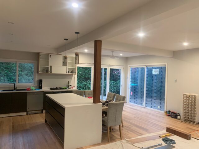 Open-plan kitchen and dining under renovation with island, timber floors, sliding glass doors.