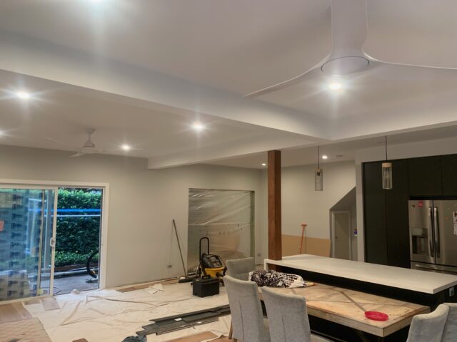Kitchen and dining renovation with island bench, pendant lights, drop sheets, tools, and sliding door.