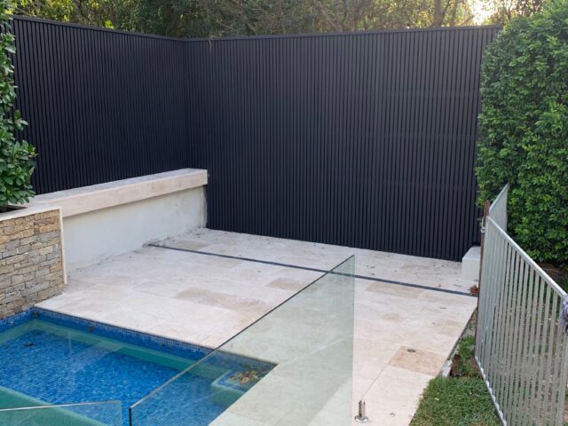 Blue-tiled swimming pool with stone paving, frameless glass fence and black slat privacy screen.