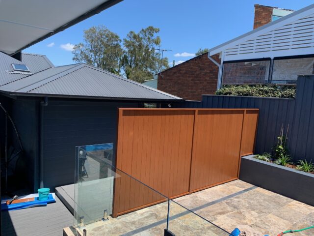 Backyard renovation with timber privacy screen, glass balustrade, composite deck and tiled patio.