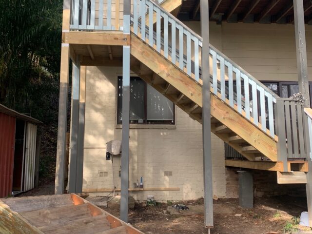 Elevated timber deck and staircase with grey balustrade, support posts over cleared backyard.