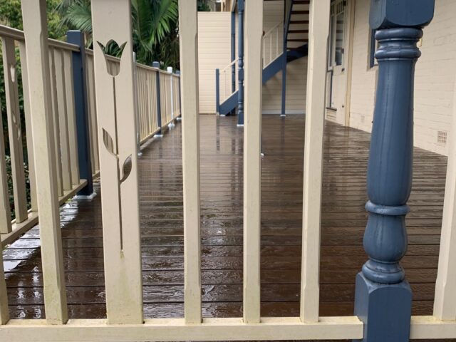 Rain-soaked timber deck with cream balustrade and blue posts, stairs and palm trees.