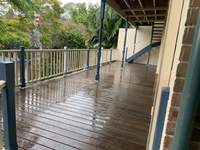 Rain-soaked timber deck with cream balustrade, external stair, and garden views.