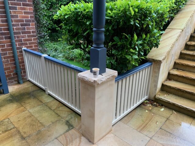 White slatted garden fence with blue capping beside sandstone steps and hedges.