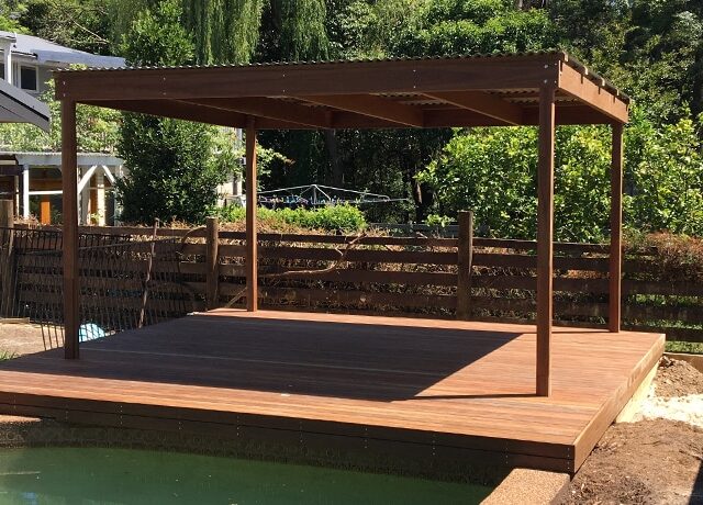 Timber deck with freestanding pergola beside backyard pool and garden